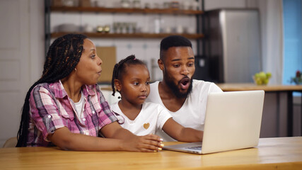 Happy african family with kid sit at table using laptop and giving high five