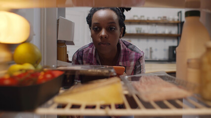 Afro-american woman looking inside refrigerator making grocery shopping list on mobile phone app