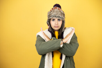 Young beautiful woman wearing a hat and a green winter coat over yellow background Rejection...