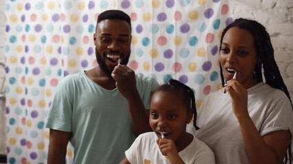 Happy african family brushing teeth together in bathroom standing in front of mirror