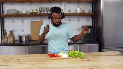 Positive african man listening to music and cooking vegetables in kitchen