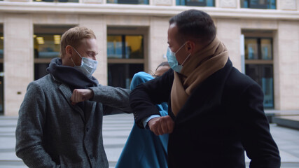 Coworkers in protective face masks elbow bumping greeting outdoors