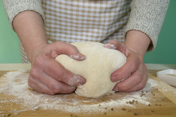 Grandma kneads dough on the table to make homemade bread with spices