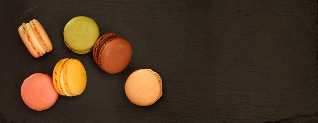 Macaroons in assortment green, yellow, cream, pink, brown with different fillings on black plate