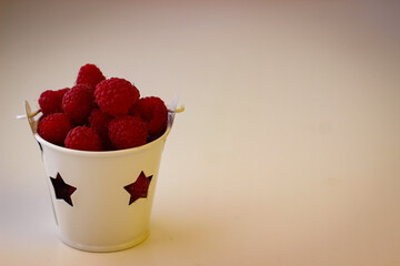 Red ripe and juicy raspberry in a small white bucket with stars