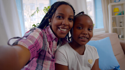 Happy african mother and little daughter making video call at home
