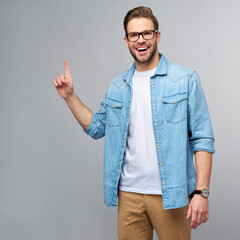 Happy young handsome man in jeans shirt pointing away standing against grey background