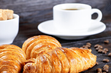 Croissants and cup of coffee on a brown wooden background, Breakfast with croissants and coffee. Morning coffee and pastry.Coffee beans and cane sugar.