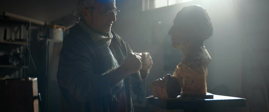 Portrait of senior adult middle eastern male sculptor working on a bust project in his home garage workshop. Retirement hobby concept. Shot with 2x anamorphic lens