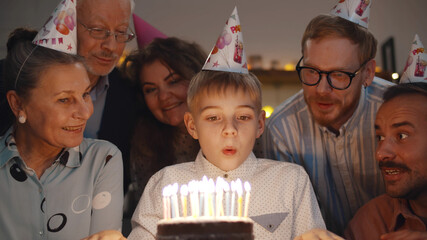 Cute boy blowing out birthday cake candles at family party - Powered by Adobe