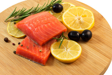 Pieces of lightly salted red fish with lemon, olives, spices on a cutting kitchen board.