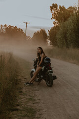 Young woman leaning on a motorcycle on dirt road next to golden grass,
Fashion Campaign, Tourist Advertising, Travel, Nature, Mechanic, Motorbike, Woman
