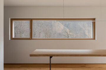 Detail of wooden table with design lamp and window to the forest of the Swiss Alps