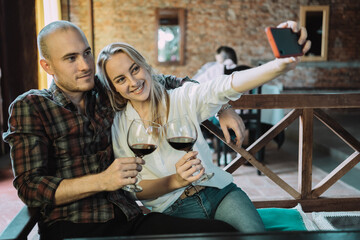 A smiling young Caucasian couple enjoying their date - Young couple toast with glasses of wine while taking out a selfie.