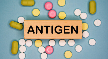 ANTIGEN written on wooden block on a blue background among multicolored pills. Medical concept