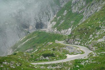 Mist rolls down along the grassy hills and empty road of a mountain in the Alps.