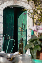 Green wooden door  ajar, old country house with a dining table and a chair in the  blurred foreground.
