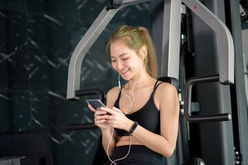 Obraz na płótnie Canvas Beautiful smiling woman in earphones using a social network and listening to music at gym, Fitness and technology concept