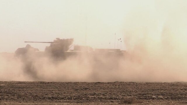 An armored personnel carrier drives through the sand in the desert, raising a cloud of dust. Concept: war zone in the east, movement of military equipment.