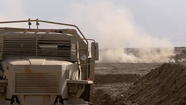 An armored personnel carrier drives through the sand in the desert, raising a cloud of dust. Concept: war zone in the east, movement of military equipment.