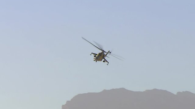 A combat Russian military helicopter is flying in the desert sky between the mountains, attacking the enemy from the air.