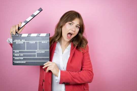 Young business woman over isolated pink background holding clapperboard very happy having fun