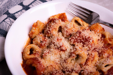 Cooked Italian Tortellini in Red Tomato Sauce with Cheese In White Bowl on Marble Surface with Graphic Napkin