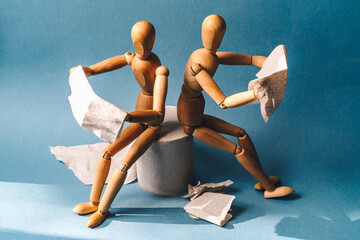 Wooden figure sit on a roll of toilet paper and reading the newspaper