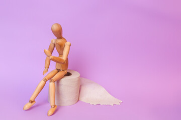 Wooden figure sit on a roll of toilet paper. Concept of the problem with digestion.
