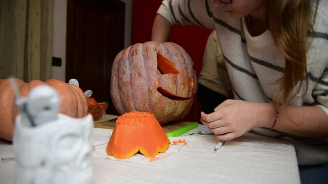 4K Father and daughter carving pumpkin, Jack o lanterns on Halloween in the kitchen. Celebrating Halloween at home with a Creepy Pumpking, fall family tradition