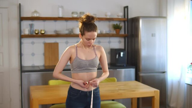 Young woman checking dieting success by measuring her waist with measuring tape