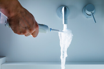 hand holding toothbrush under flowing water from faucet in a hospital