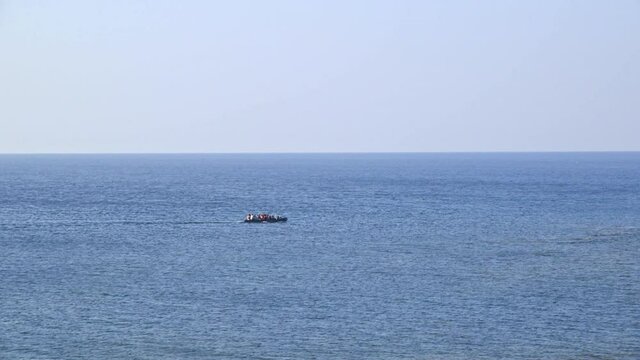 Refugees in rubber boat float in the middle of the ocean.