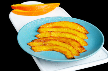 Yellow slices of fried pumpkin on a blue plate, isolated on a black background. Selective focus