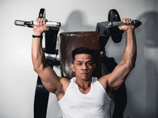 A serious and focused asian fitness buff lifts on the shoulder press machine. Working out shoulders...
