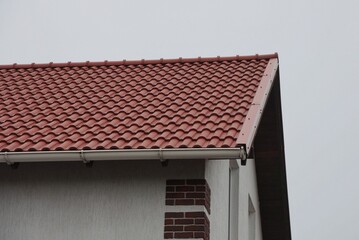 Obraz premium part of brown tiled roof and gray wall of a private house on the street against the background of the sky