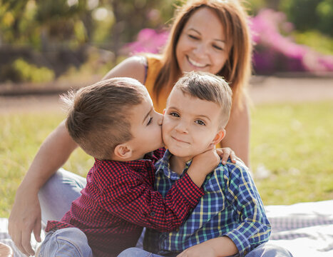 Little Boy Kissing His Twin Brother - Mother In The Background - Happy Family Enjoy A Pic Nic In A Nature Park - Mother And Child Love