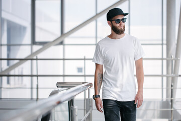 Hipster handsome male model with beard wearing white blank t-shirt and a baseball cap with space...