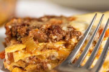 Baked Lasagne in Glass Pan Served on White Plate with Fork and Napkin on Wood Surface