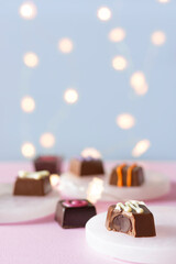 Hand decorated chocolate candy bonbons and pralines desserts on pink and blue background with lights