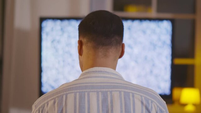 Back view of man sitting in front of tv with no signal