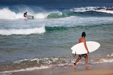 surfer walk along the shore of Maroubra beach with his board, lwhile observing the other surfers...