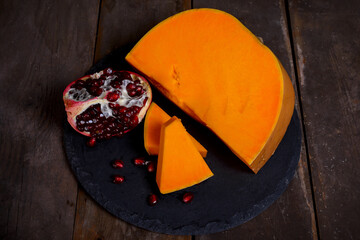 Sliced pumpkin with pomegranate on a wooden background.