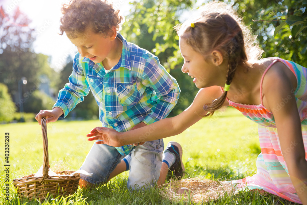 Wall mural Cute boy and girl celebrating Easter, searching and eating chocolate eggs. Happy family holiday. Happy kids laughing, smiling and having fun. Beautiful spring sunny day in park