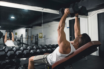 A man in white tank top does some incline dumbbell flys. Working out, training chest with an...