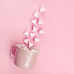 Marshmallows in the shape of hearts flying out of pink cup.