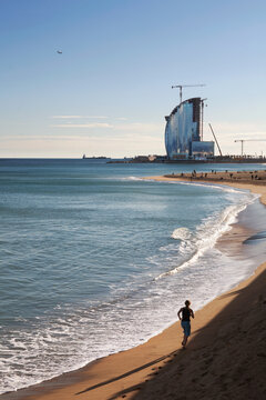 Woman running alone the seashore of  Barceloneta beach, with the stunning W Barcellona hotel in the background, Barcelona, Spain, Europe.