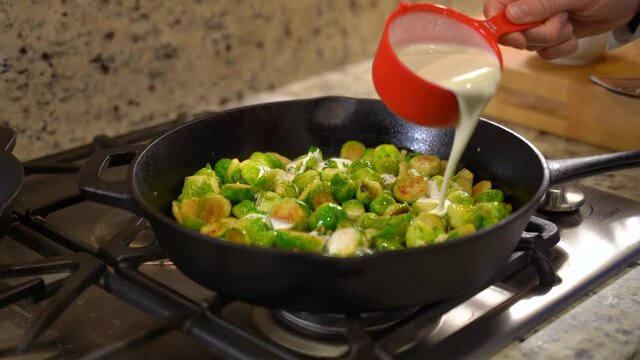 Cooking Roasted Sautéed Brussels Sprouts in a Cast Iron Pan Skillet - Pouring Cream out of Measuring Cup - Wide Shot