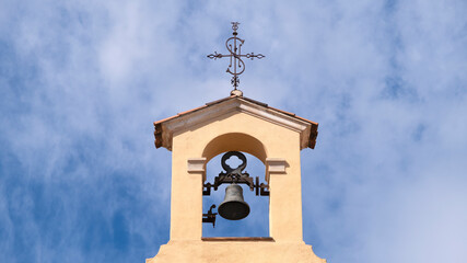 Small rural village church detail. Bell tower and a cross against a blue sky. Empty copy space for Editor's content.