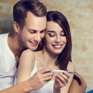 Happy couple, finding out results of a pregnancy test, over loft style wall. Love, relationship, dating, happy lovers concept picture. Square composition.